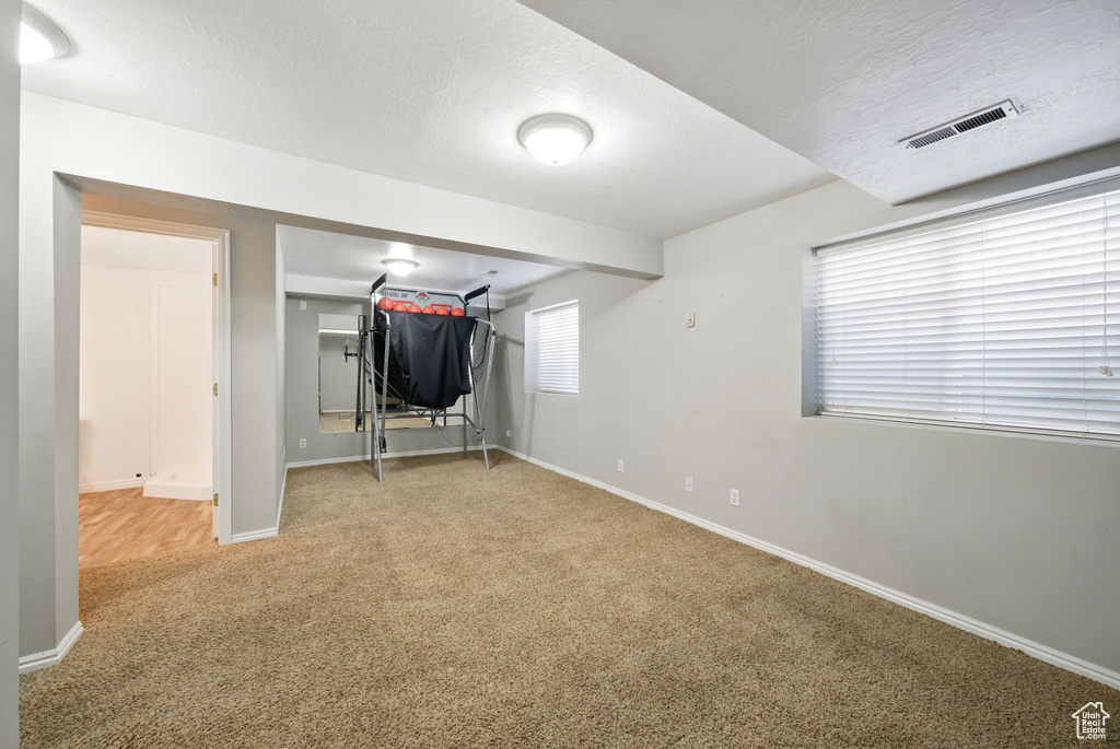 Basement with carpet floors, baseboards, a textured ceiling, and visible vents