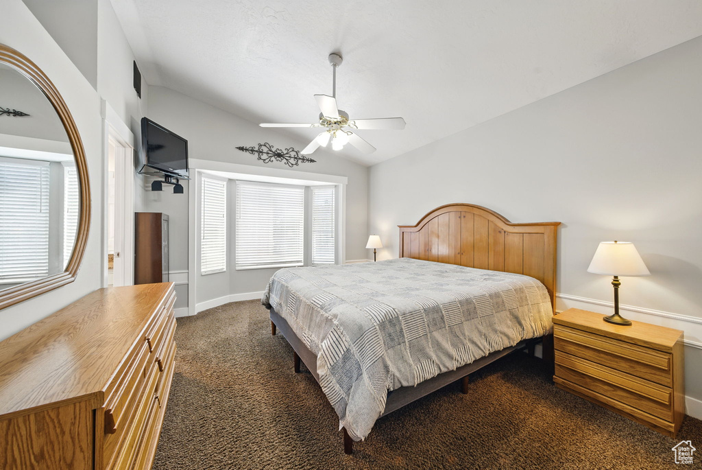 Bedroom featuring a ceiling fan, visible vents, vaulted ceiling, baseboards, and dark carpet