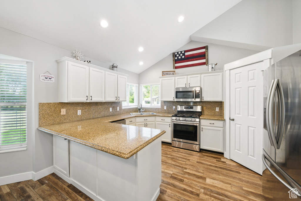 Kitchen featuring decorative backsplash, a peninsula, white cabinets, a sink, and appliances with stainless steel finishes