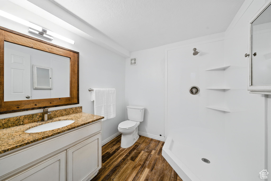 Full bathroom featuring vanity, toilet, baseboards, wood finished floors, and a shower