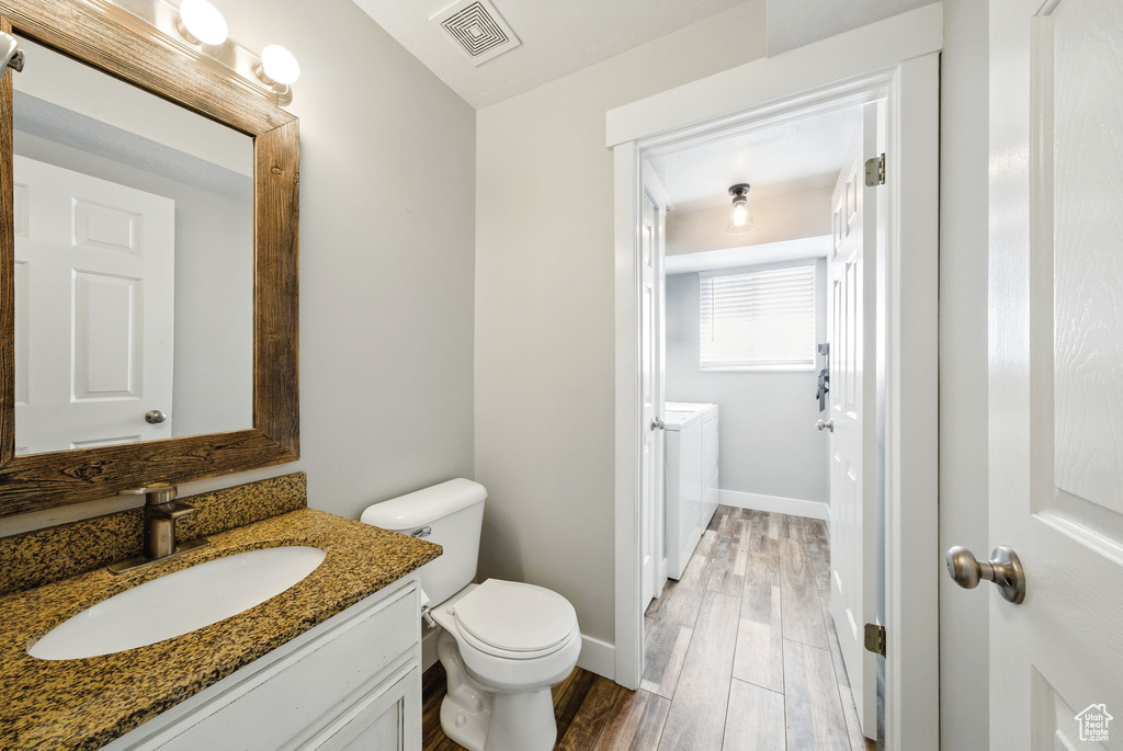 Bathroom with washing machine and clothes dryer, vanity, toilet, wood finished floors, and visible vents