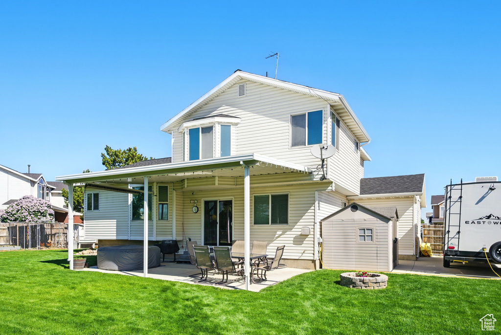 Rear view of house featuring a fire pit, fence, a patio, a lawn, and a hot tub