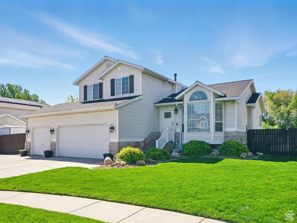 Split level home featuring fence, stone siding, a garage, a front yard, and concrete driveway
