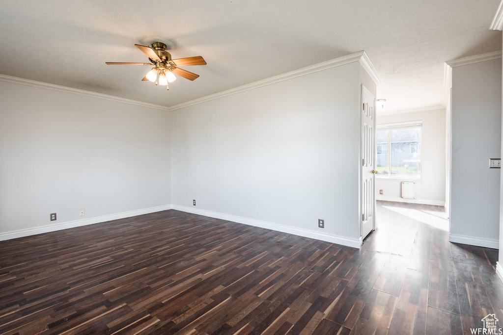Empty room featuring a ceiling fan, dark wood-type flooring, crown molding, and baseboards