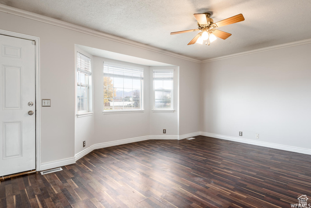 Spare room with dark wood-style floors, baseboards, crown molding, and a ceiling fan