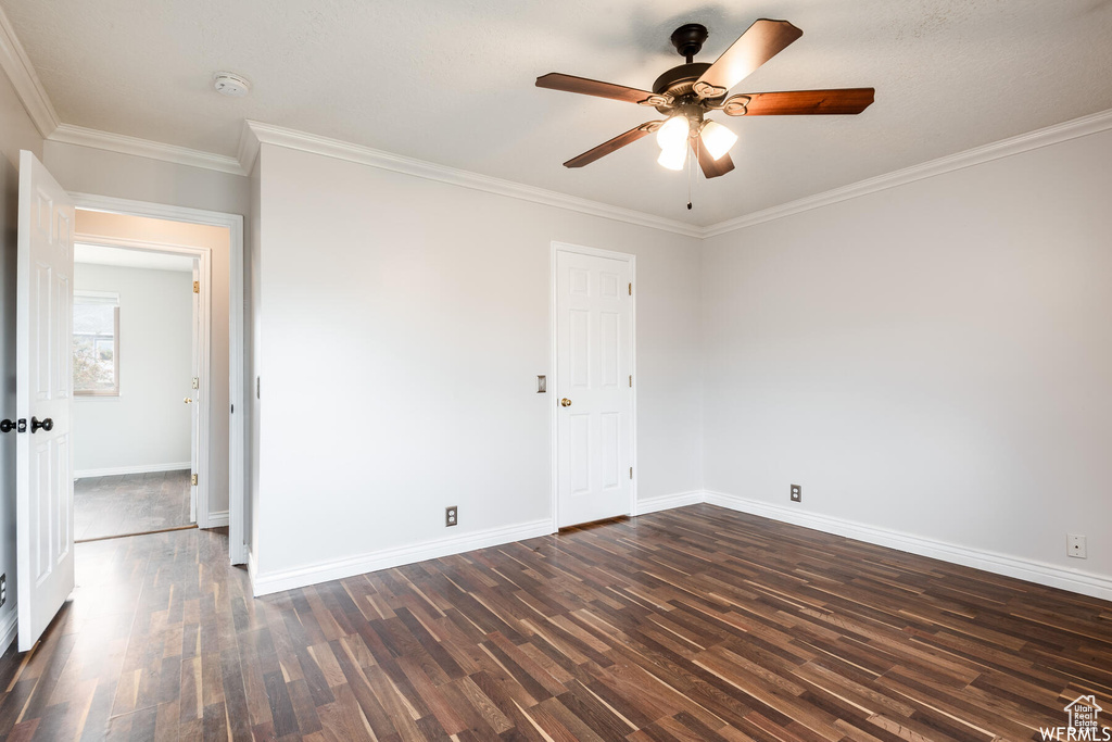 Empty room featuring dark wood-style flooring, baseboards, and ornamental molding