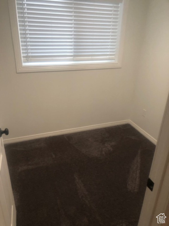 Empty room with dark colored carpet, baseboards, and a wealth of natural light