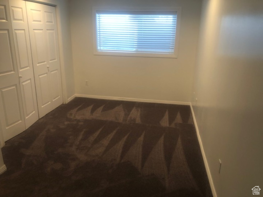 Unfurnished bedroom with dark colored carpet, baseboards, and a closet