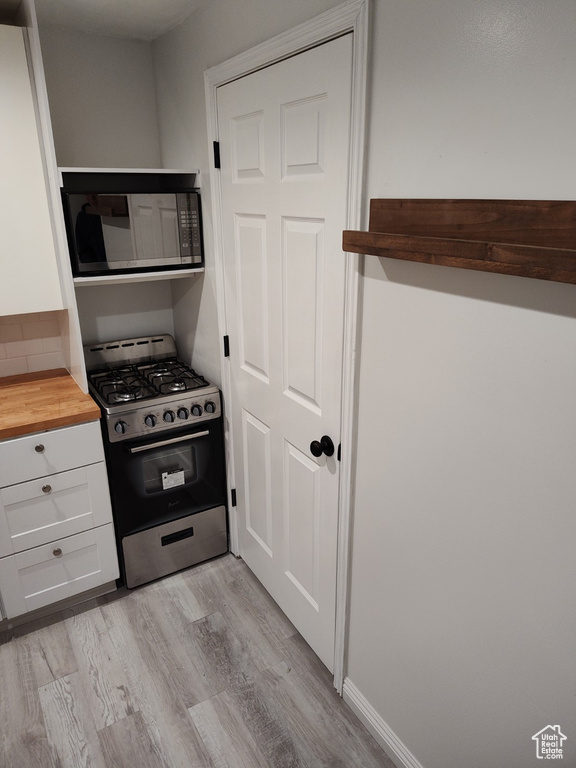 Kitchen with black microwave, white cabinets, butcher block counters, and gas range