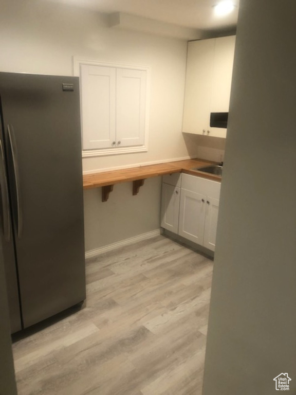 Kitchen featuring freestanding refrigerator, wooden counters, light wood-style floors, baseboards, and white cabinets