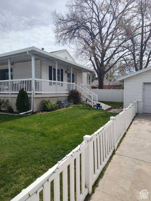 Exterior space with a porch, concrete driveway, a fenced backyard, and a front lawn