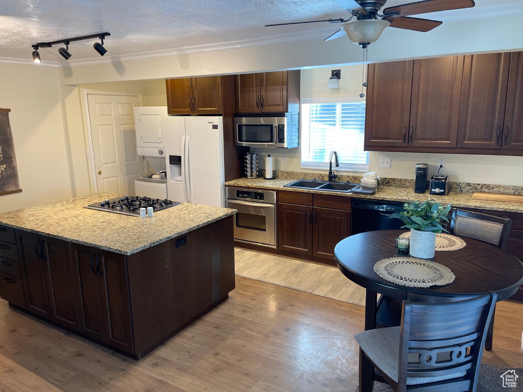 Kitchen with a ceiling fan, stacked washer / dryer, appliances with stainless steel finishes, rail lighting, and a sink