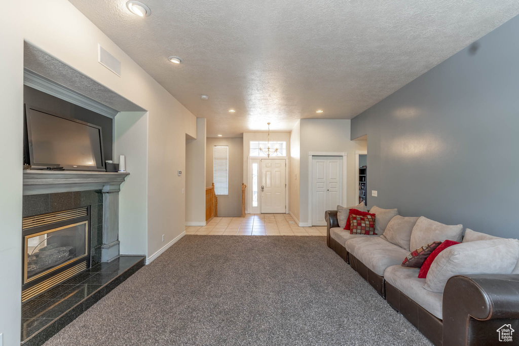 Living room featuring carpet floors, baseboards, a textured ceiling, a chandelier, and a tiled fireplace