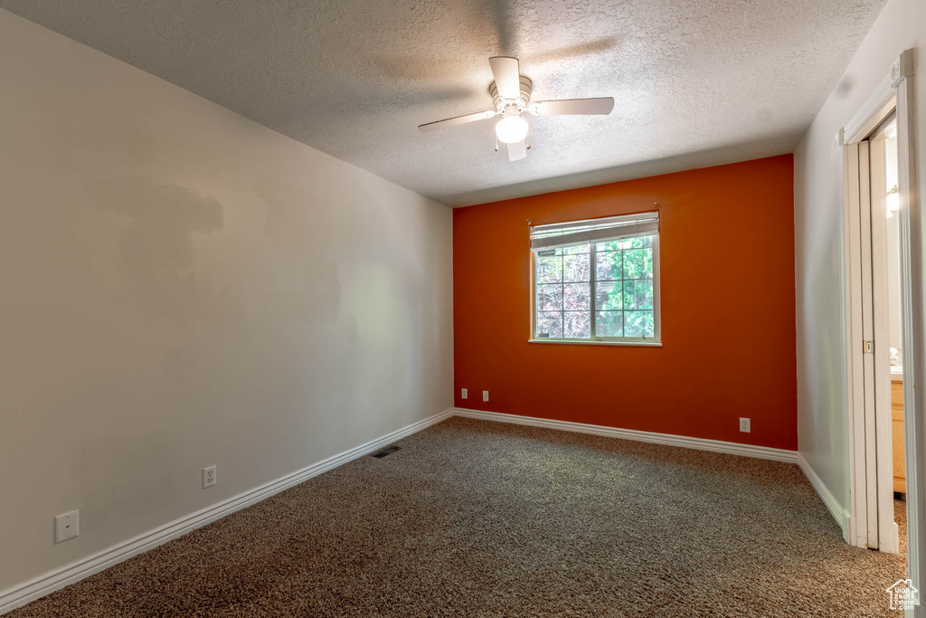 Empty room with carpet flooring, a textured ceiling, a ceiling fan, baseboards, and visible vents