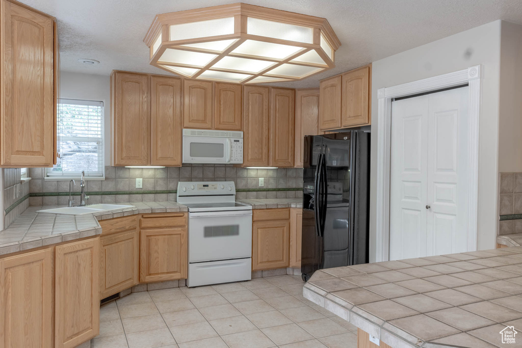 Kitchen with tile countertops, light brown cabinetry, tasteful backsplash, a sink, and white appliances