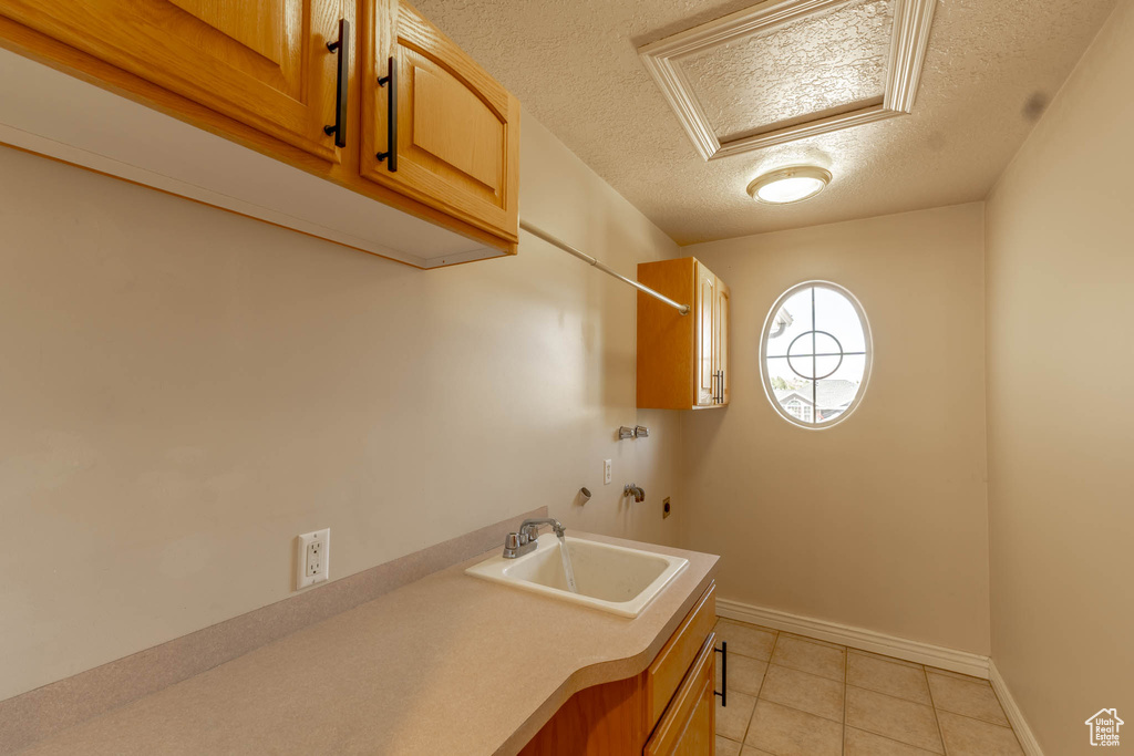 Washroom with a textured ceiling, a sink, cabinet space, light tile patterned floors, and washer hookup