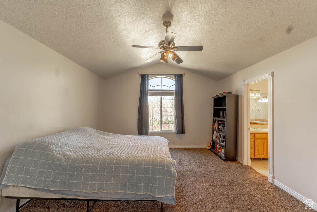 Carpeted bedroom featuring baseboards, ensuite bathroom, a textured ceiling, a ceiling fan, and vaulted ceiling
