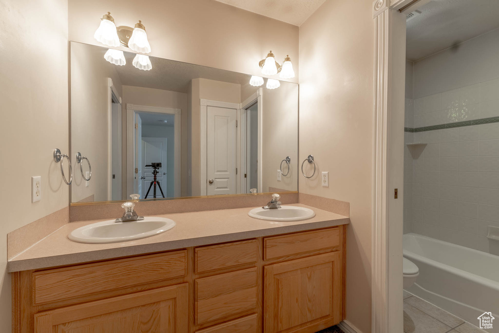 Bathroom with double vanity, a sink, tile patterned floors, and toilet