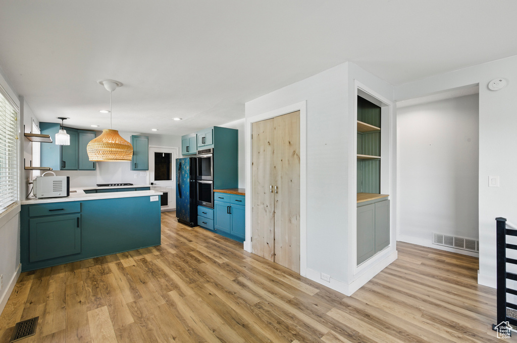 Kitchen featuring stovetop, visible vents, light wood-type flooring, light countertops, and a peninsula