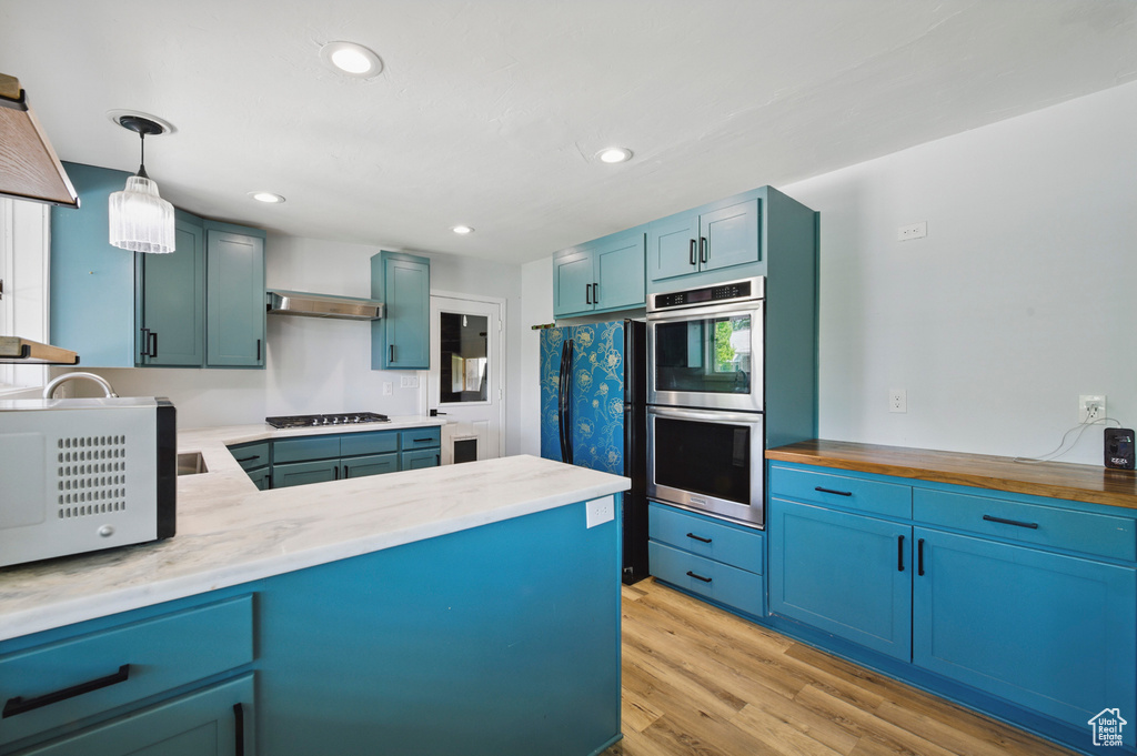 Kitchen featuring stainless steel double oven, hanging light fixtures, light wood finished floors, recessed lighting, and white microwave