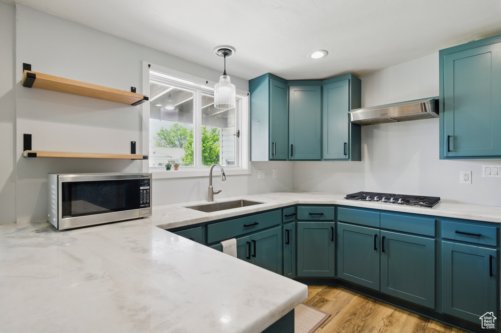 Kitchen with open shelves, ventilation hood, a sink, light wood finished floors, and appliances with stainless steel finishes