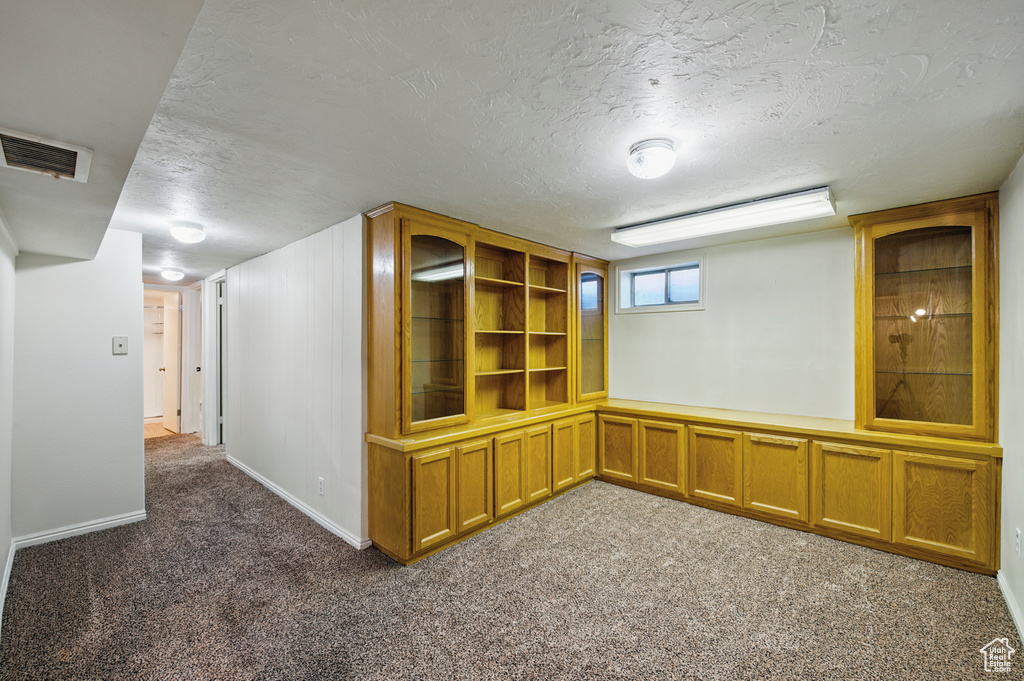 Basement featuring dark colored carpet, a textured ceiling, a decorative wall, and visible vents