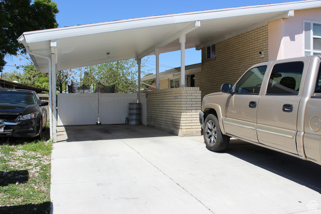 View of parking featuring concrete driveway, fence, and a carport