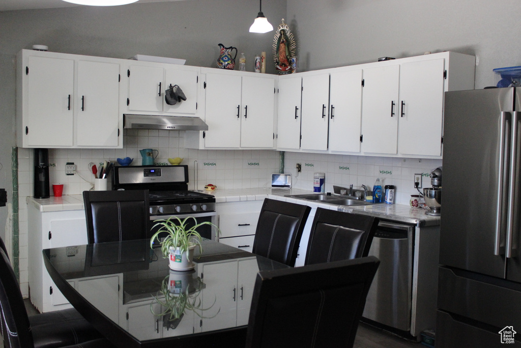Kitchen featuring under cabinet range hood, appliances with stainless steel finishes, decorative backsplash, and a sink
