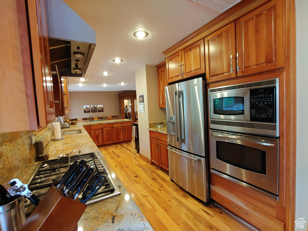 Kitchen featuring appliances with stainless steel finishes, a sink, brown cabinetry, light wood-style flooring, and recessed lighting
