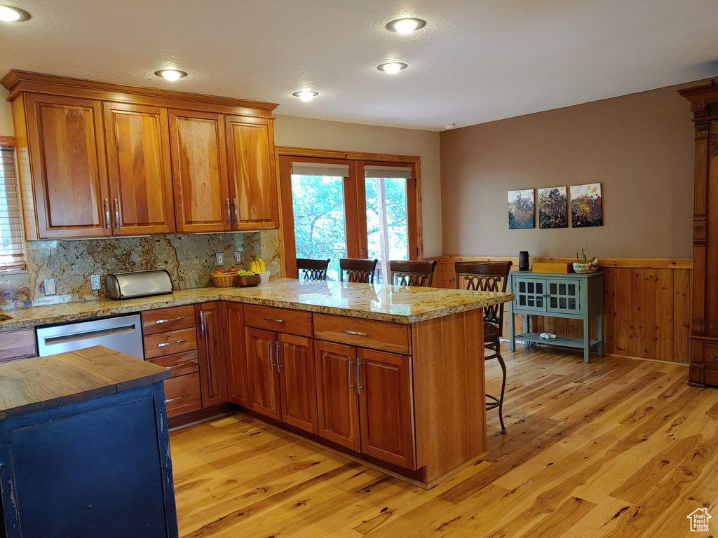 Kitchen featuring light wood-style flooring, dishwasher, a breakfast bar, and a wainscoted wall
