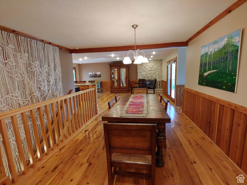 Dining space with an inviting chandelier, wainscoting, a stone fireplace, light wood-type flooring, and ornamental molding
