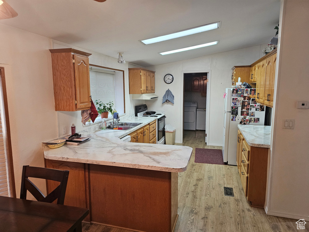 Kitchen with electric range, independent washer and dryer, light wood-type flooring, light countertops, and freestanding refrigerator