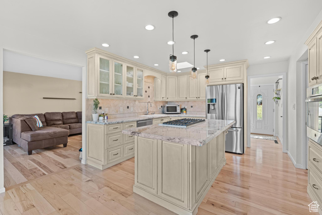 Kitchen with cream cabinets, light stone countertops, light wood-style flooring, stainless steel appliances, and tasteful backsplash