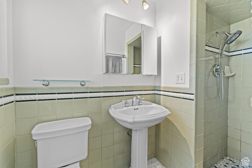 Bathroom with toilet, tile walls, a tile shower, and a wainscoted wall