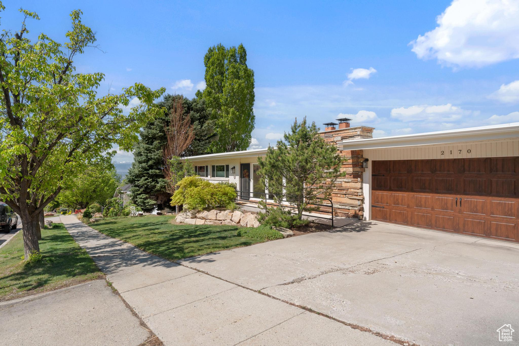 Single story home featuring a garage, a front lawn, and concrete driveway