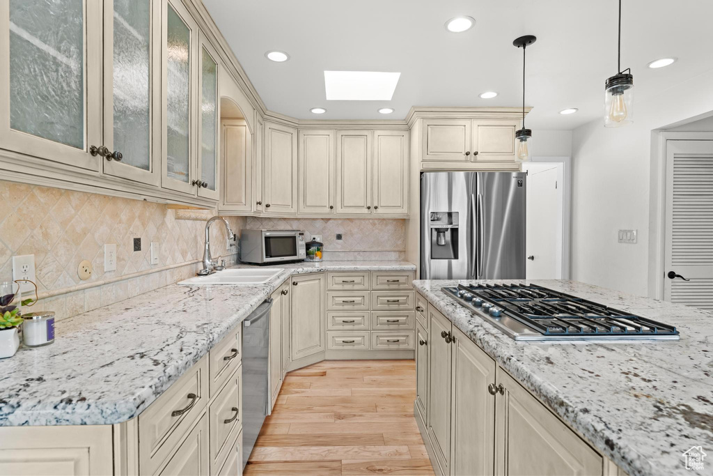 Kitchen with a skylight, cream cabinets, a sink, light wood-style floors, and stainless steel appliances