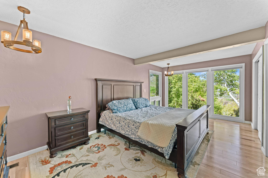 Bedroom with an inviting chandelier, a textured ceiling, baseboards, and light wood-style floors