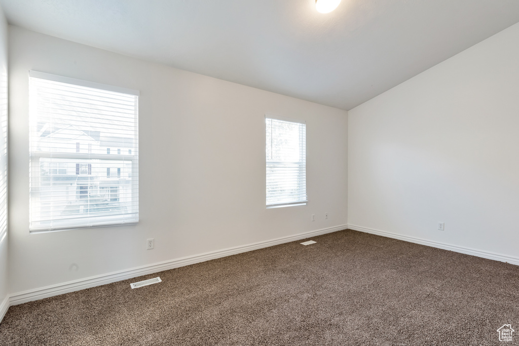 Carpeted empty room featuring baseboards, visible vents, and vaulted ceiling