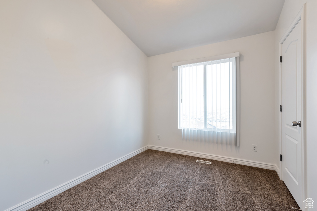 Spare room featuring baseboards, vaulted ceiling, dark carpet, and visible vents