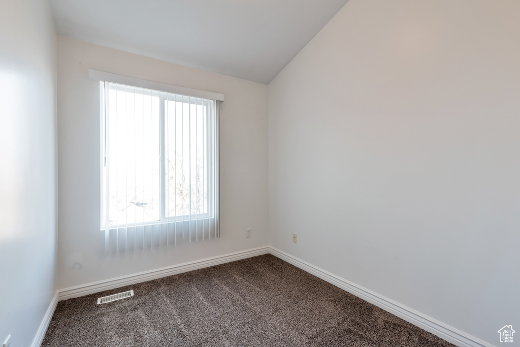 Spare room featuring baseboards, lofted ceiling, dark colored carpet, and visible vents