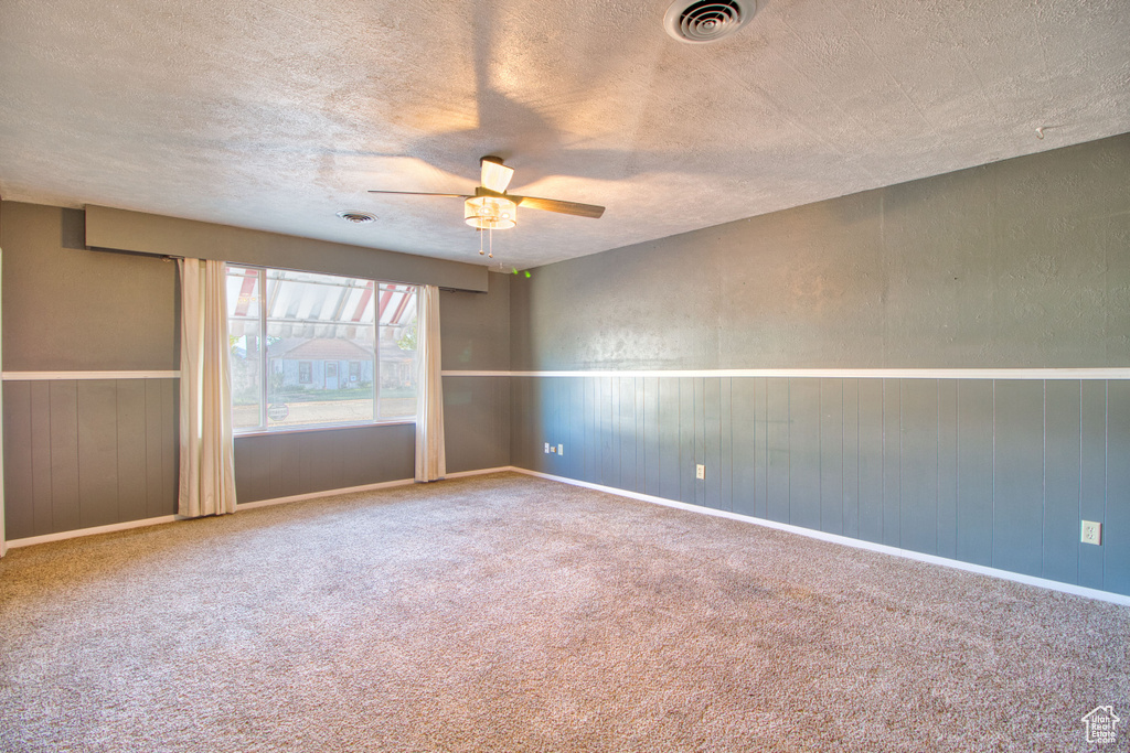 Carpeted empty room featuring visible vents, a ceiling fan, a textured ceiling, and a wainscoted wall