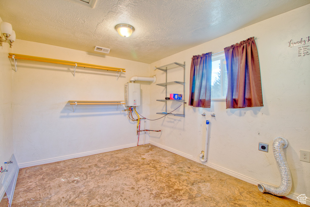 Laundry area with laundry area, baseboards, a textured ceiling, water heater, and hookup for an electric dryer