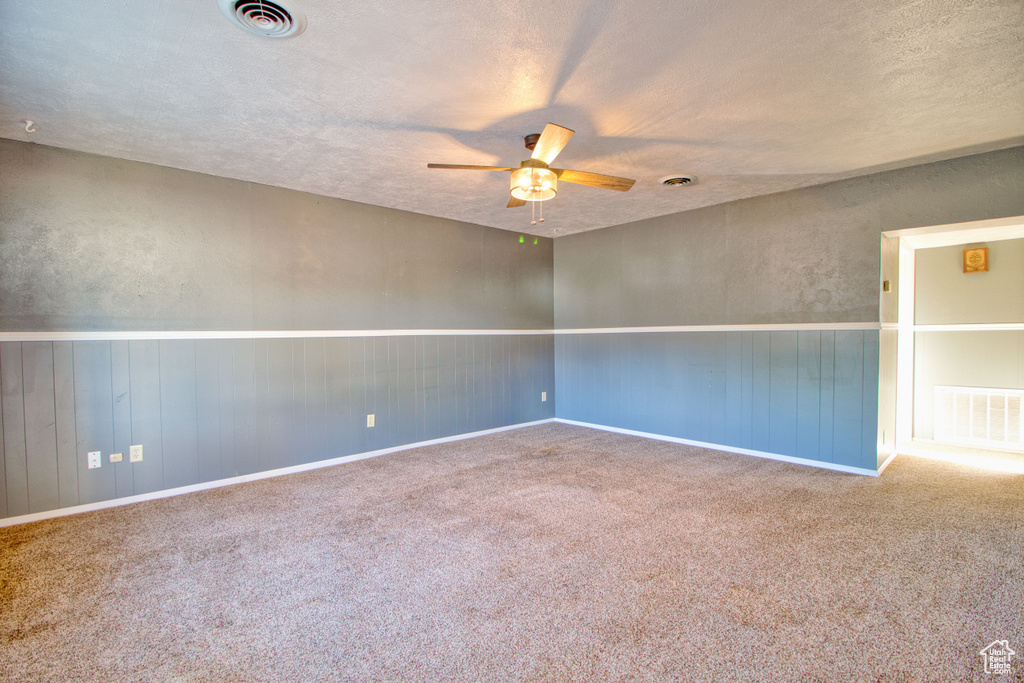 Carpeted empty room featuring visible vents, a ceiling fan, baseboards, and a textured ceiling