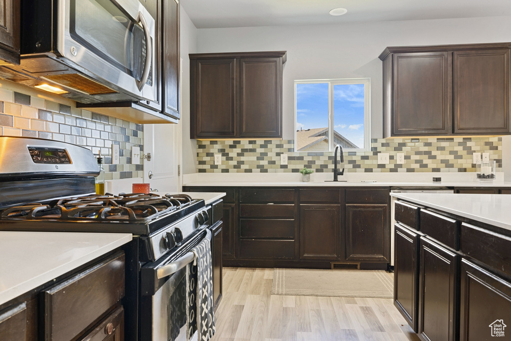 Kitchen featuring dark brown cabinets, light wood-style floors, light countertops, a sink, and stainless steel appliances