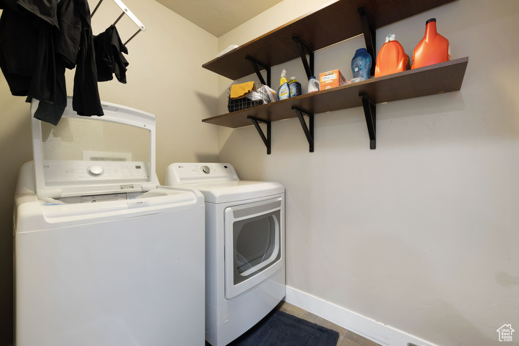 Clothes washing area with laundry area, baseboards, tile patterned floors, and washer and dryer