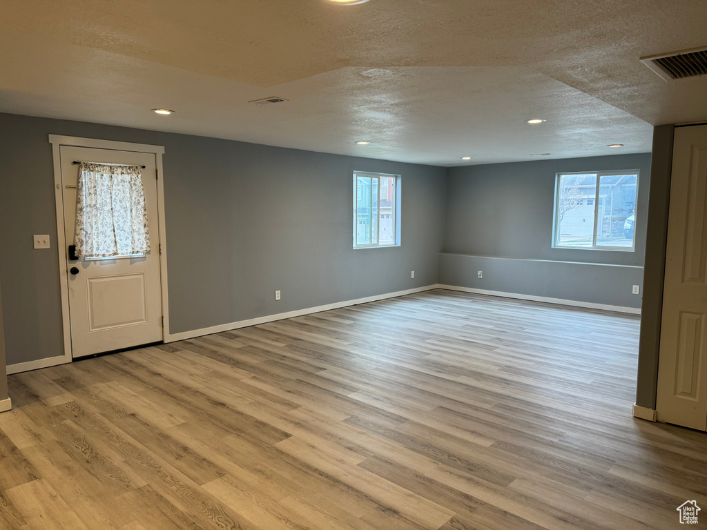 Interior space featuring a textured ceiling, visible vents, baseboards, and wood finished floors