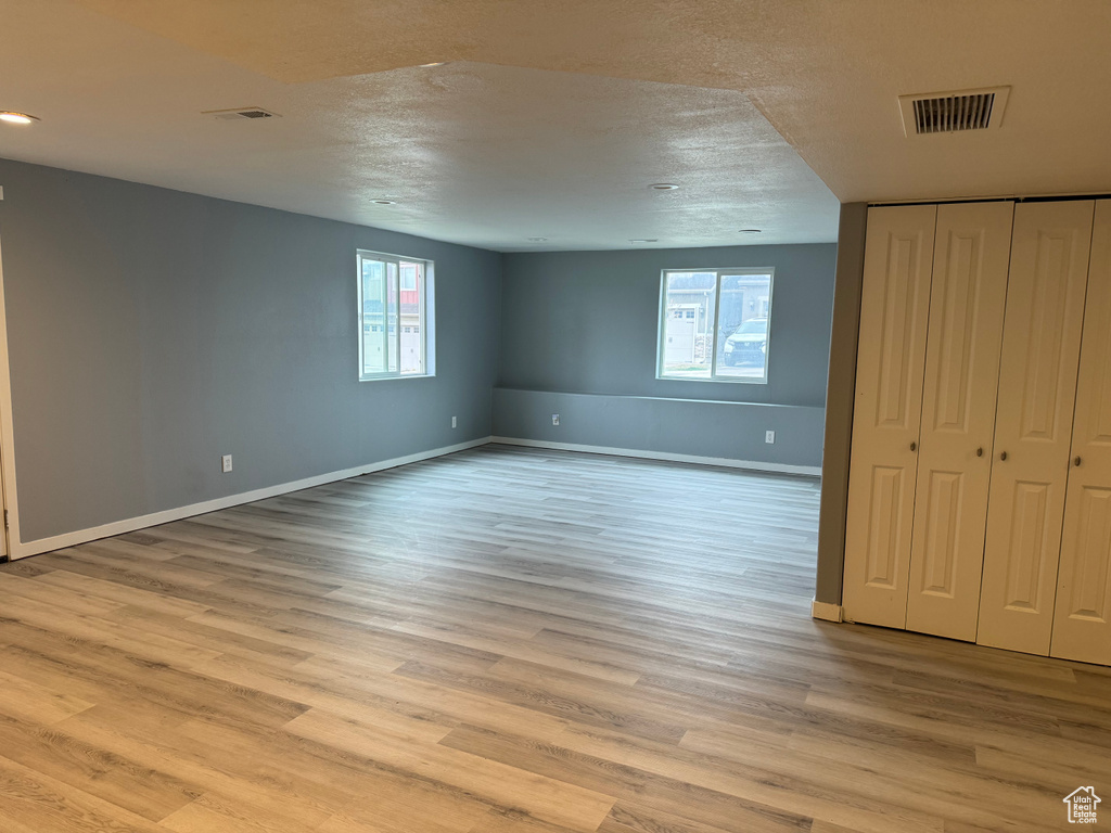 Basement with baseboards, plenty of natural light, light wood-style flooring, and visible vents