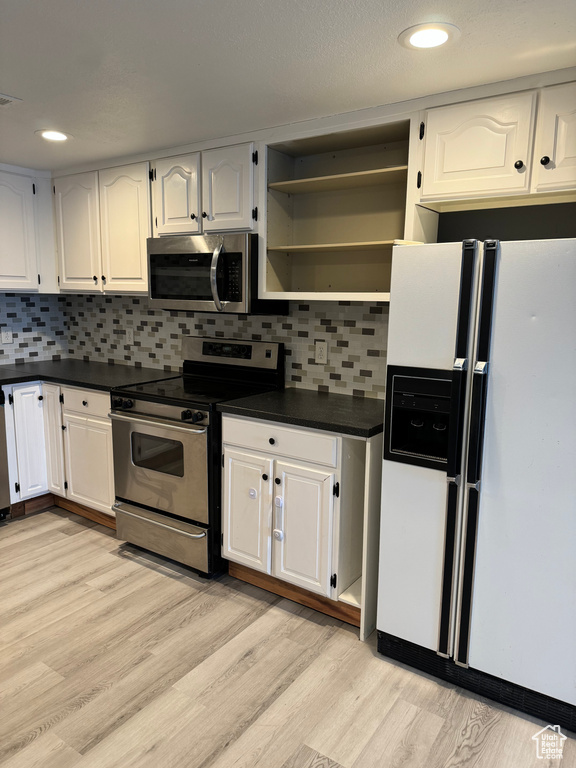 Kitchen featuring dark countertops, tasteful backsplash, white cabinets, light wood-style floors, and stainless steel appliances