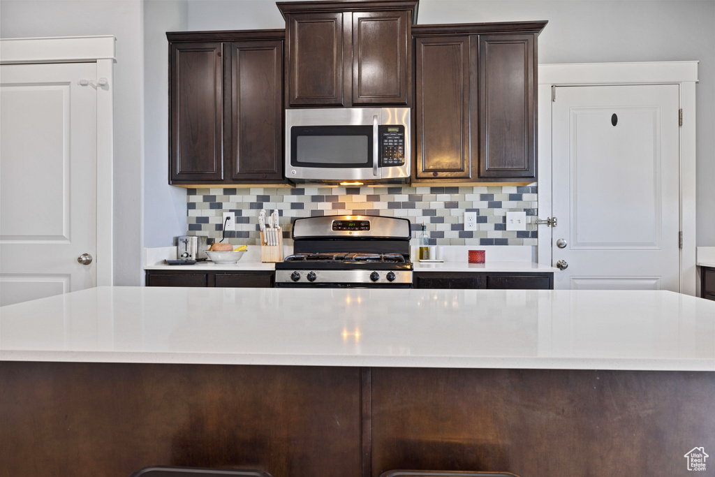 Kitchen featuring light countertops, decorative backsplash, dark brown cabinets, and stainless steel appliances