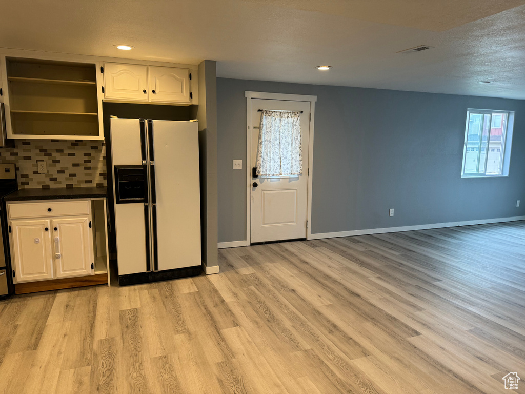 Kitchen with white cabinets, white refrigerator with ice dispenser, light wood-style floors, baseboards, and tasteful backsplash